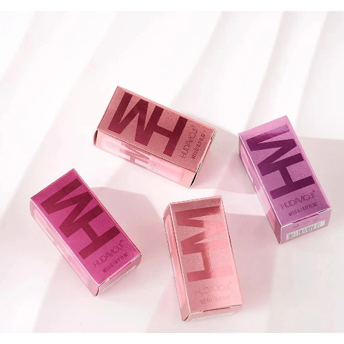HUDA MOJI colorful lipstick collection featuring pink, coral, and red lipstick tubes with matching product packaging arranged on a soft pastel background.