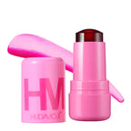 HUDA MOJI colorful lipstick collection featuring pink, coral, and red lipstick tubes with matching product packaging arranged on a soft pastel background.