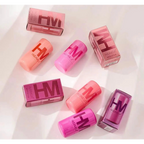 HUDA MOJI colorful lipstick collection featuring pink, coral, and red lipstick tubes with matching product packaging arranged on a soft pastel background.