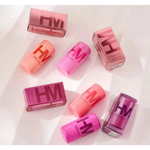 HUDA MOJI colorful lipstick collection featuring pink, coral, and red lipstick tubes with matching product packaging arranged on a soft pastel background.