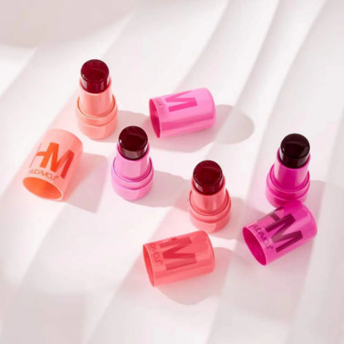 HUDA MOJI colorful lipstick collection featuring pink, coral, and red lipstick tubes with matching product packaging arranged on a soft pastel background.